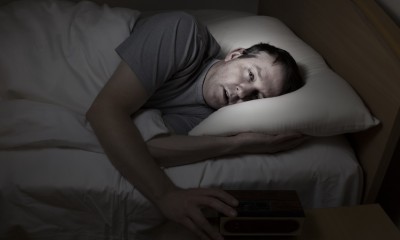 Mature man, eyes wide open with hand on alarm clock, cannot sleep at night from insomnia