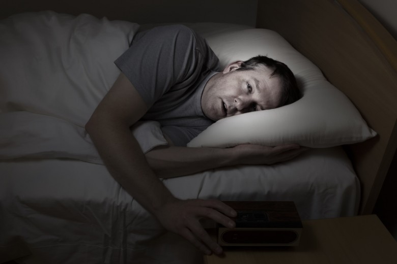 Mature man, eyes wide open with hand on alarm clock, cannot sleep at night from insomnia